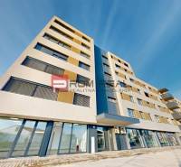 A building with commercial spaces on Obchodná Street in Pezinok, under a blue sky.