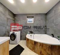 A bathroom with a bathtub and a washing machine in a family house. Gray walls with light floors.