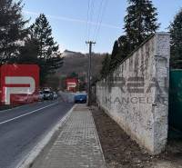 A path with a sidewalk leading through Pezinok by a family house, with hilly landscape in the background.