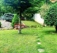 The garden of a family house in Píla with trees, grass, and a rockery.