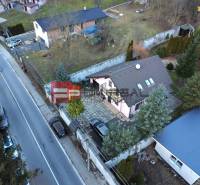 A family house in Píla by the road, with two cars and a landscaped garden.