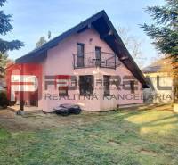 A family house in Píla with an attic roof, a balcony, and a garden surrounded by trees.