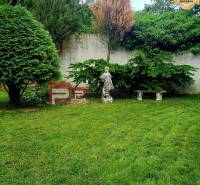 The garden of a family house in the village of Píla with a lawn, a statue, and a bench by the wall.