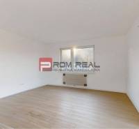 A room in a two-room apartment with white walls and wooden flooring.