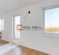 A bright room with wooden flooring and large windows in a 2-room apartment.
