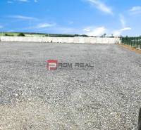 Gravel area in the production premises in Pezinok, bordered by a fence and a concrete wall.