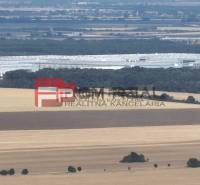 Countryside with agricultural land near Senecká Street, distant industrial buildings.