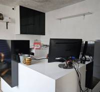 An office with a desk, monitor, and shelves, located on Partizánska Street near the warehouses.