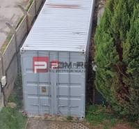 On Púchovská Street in Bratislava III, there is a shipping container next to greenery and a fence.