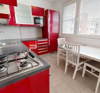 Kitchen of a 4-room apartment with red cabinets, a gas stove, and a dining table.