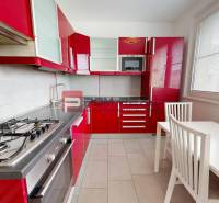 A kitchen with red cabinets, a gas stove, and a white dining table in a four-room apartment.