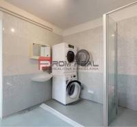 A bathroom in a family house with a washing machine, dryer, and shower stall.