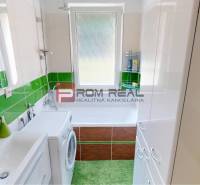 The bathroom of a 3-room apartment with a white washbasin cabinet and green tiles.
