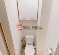 A toilet in a 3-room apartment with a storage cabinet above the flush tank.