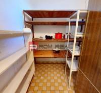 A pantry in a family house with shallow shelves and pots on a tiled floor.