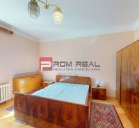 A bedroom in a family house with antique furniture, wooden flooring, and a large window.