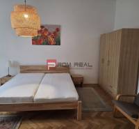 Bedroom in a 2-room apartment with wooden furniture, chandeliers, and a painting with flowers.
