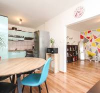 Kitchen and living room in a 3-room apartment with a colorful geometric wall and a dining table.