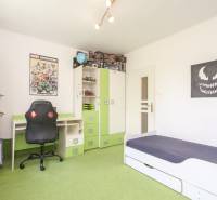 Children's room in a three-room apartment with a bed, desk, chair, and wall decorations.