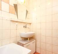 A bathroom in a 3-room apartment with a bathtub and a sink in beige tiles.