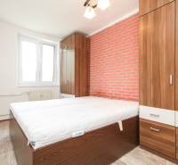 A bedroom in a 3-room apartment with a brick wall, wooden furniture, and a window.
