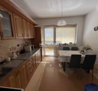 A kitchen in a 3-room apartment with a dining table, cabinets, and balcony doors.