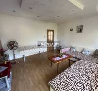 Living room in a three-room apartment with wooden flooring and simple furniture.