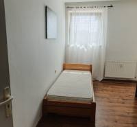 A single bed in a room with a window and a curtain in a 2-room apartment.
