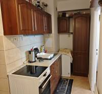 A kitchen in a 2-room apartment with a stove, sink, and wooden cabinets.