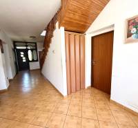 Hallway in a family house with a wooden staircase, tiles, and a vase with flowers on the wall.