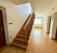 Interior of a family house with a wooden staircase, a tiled hallway, and a window that illuminates the space.