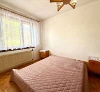 Bedroom with a bed, window, and wooden floor in a family house.