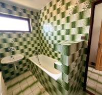 A bathroom in a family house with green tiles, a bathtub, and a sink.