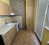 A kitchen with wooden cabinets, a stove, and a sink in a studio apartment.