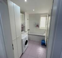 A bathroom in a 2-room apartment with a washing machine, bathtub, sink, and storage spaces.