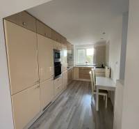 A kitchen in a 2-room apartment with white furniture and wooden flooring.