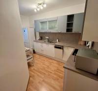 A kitchen in a 2-room apartment with wooden flooring, white furniture, and appliances.