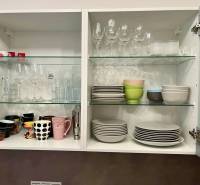 An open kitchen cabinet with glasses, cups, and plates in a 2-room apartment.