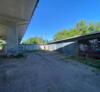 Garages in Zvolen under the bridge with graffiti on the walls and a parked car.