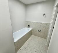 Bathroom in a 2-room apartment with a bathtub and light ceramic tiles.