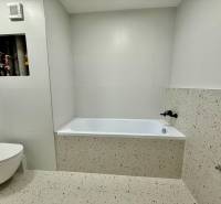 Bathroom with a bathtub and toilet in a 2-room apartment with white tiles.