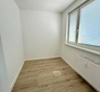 A room with light walls, wooden flooring, and a large window in a 2-room apartment.