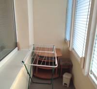 Glazed balcony in a 2-room apartment with a shelf, clothes dryer, and trash bin.