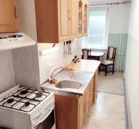 A kitchen in a 2-room apartment with a gas stove, sink, and wooden cabinets.