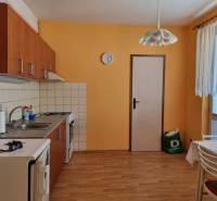 A kitchen in a 2-room apartment with orange walls, wooden floor, and a dining table.