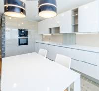 A kitchen in a 3-room apartment with a dining table, built-in appliances, and white cabinets.