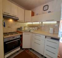 A kitchen in a family house with appliances, a sink, cabinets, a clock, and decor on the tiles.