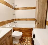 Bathroom in a studio apartment with a bathtub, washing machine, toilet, and wooden details.