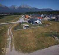 Residential plots in Mlynica with a view of the Tatras, a country house, and buildings in the background.