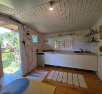 A kitchen in a cottage with white walls, wooden floor, and colorful decorations on the doors.